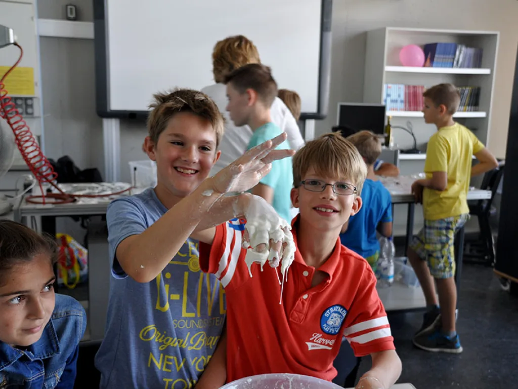 Zwei Kinder halten ihre mit Masse überzogenen Hände in die Kamera.